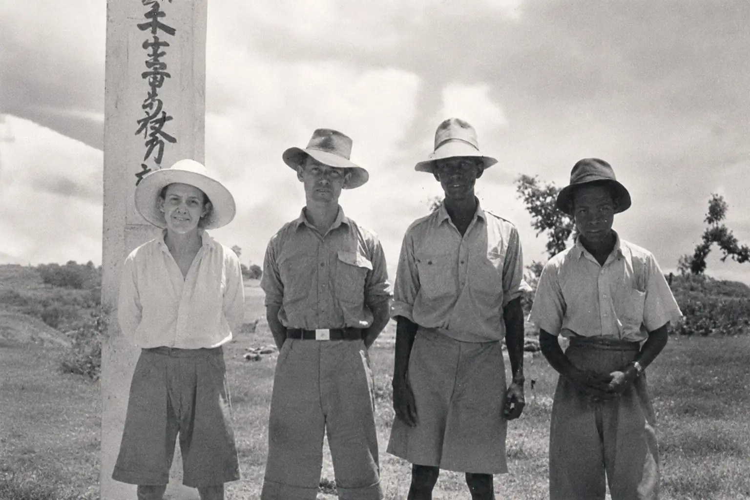 Four settlers beside a Japanese headquarters office sign